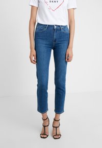 Blue denim jeans dengan potongan lurus, pinggang tinggi, dan ujung yang robek. Dipasangkan dengan kemeja putih lengan pendek dan sepatu hak hitam dengan tali.