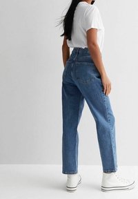 Högmidjade blå denimjeans med raka ben, med bakfickor och fransad nederkant, i kombination med vita högstövlar.