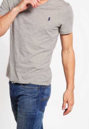 T-shirt gris en coton avec un col rond et un petit logo polo bleu marine sur la poitrine, associé à un jean en denim bleu.