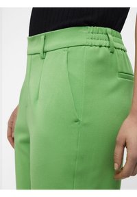 Pantalon vert extensible avec une texture lisse, un design plissé et une ceinture élastique. Comprend des poches latérales et une coupe ajustée.