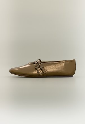 Zapato plano de bronce brillante con punta puntiaguda y dos pequeñas correas con hebilla en la parte superior sobre un fondo neutro.