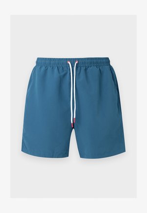 Sinised ujumispüksid elastse vöökohaga ja valge kinnitusnööriga, mille otsad on punased, esitatud tasapinnaliselt helehallil taustal.