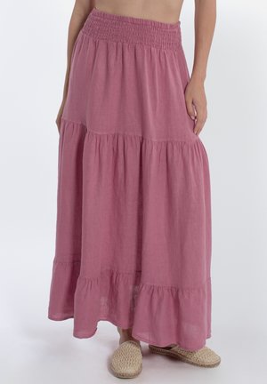 Gonna maxi lilla a balze con vita smock, indossata con scarpe slip-on intrecciate, mostrata dalla vita ai piedi su sfondo semplice.