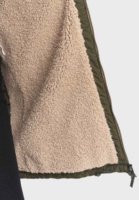 Olivengrøn yderstofjakke med en beige, fluffy fleeceforing. Lynlås-lukning og justerbar kant. Blød tekstur hele vejen igennem.