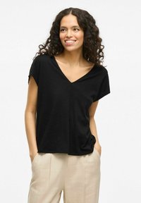 T-shirt nera a maniche corte e scollo a V con vestibilità rilassata, realizzata in un tessuto testurizzato. Abbinata a pantaloni beige chiaro.