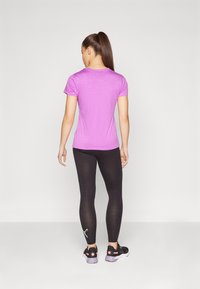 Kortärmad, figursydd, ljuslila träningsskjorta i kombination med svarta tights. Tightsen har en logo på det nedre benet och bärs med svarta skor.