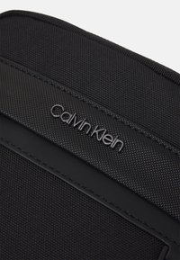 Accessorio Calvin Klein nero con tessuto testurizzato, bordi simili alla pelle liscia e dettaglio del logo in rilievo sul davanti.
