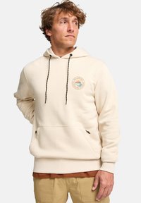 Sudadera con capucha de color crema que cuenta con un bolsillo frontal, cordones ajustables y un parche de logotipo texturizado con gráficos de sol y olas.