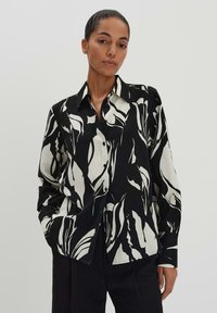 Camicia a maniche lunghe bianco e nera con un audace motivo astratto di foglie, colletto strutturato. Tessuto liscio.