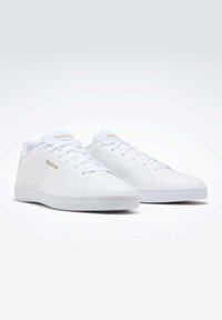 Baskets athlétiques blanches avec une tige en cuir lisse, embout arrondi, semelle plate en caoutchouc et fermeture à lacets. Logo Reebok discret dans une teinte beige.