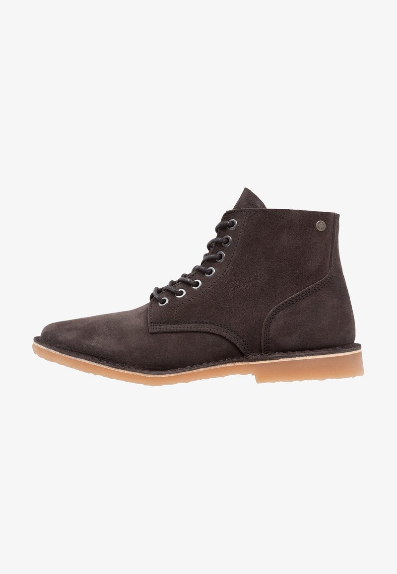 Bottines en daim marron à bout rond, avec six œillets et semelle en caoutchouc gomme. Texture lisse avec un minimum de détails métalliques.