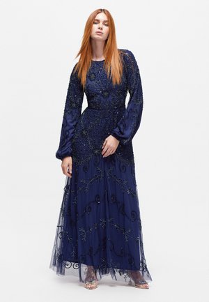 Long navy evening gown with embroidered floral patterns, sheer long sleeves, and layered tulle skirt. Beaded accents throughout.