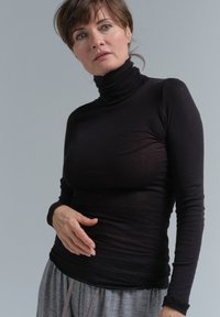 Schwarzes Rollkragenoberteil mit langen Ärmeln aus leichtem Stoff, mit einer figurbetonten Passform. Kombiniert mit grauen Schlafanzughosen, die eine weiche Textur zeigen.
