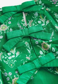 Tessuto floreale verde con tre grandi fiocchi, caratterizzato da una superficie texturizzata e da delicate fantasie floreali pastello.