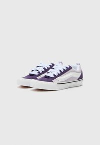 Tenisi mov și albi din piele întoarsă și țesătură, având un design low-top, șireturi albe și o bandă de accent neagră pe talpă.