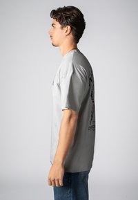 Light gray cotton t-shirt with short sleeves and a relaxed fit. Features a graphic print on the back and a crew neckline.