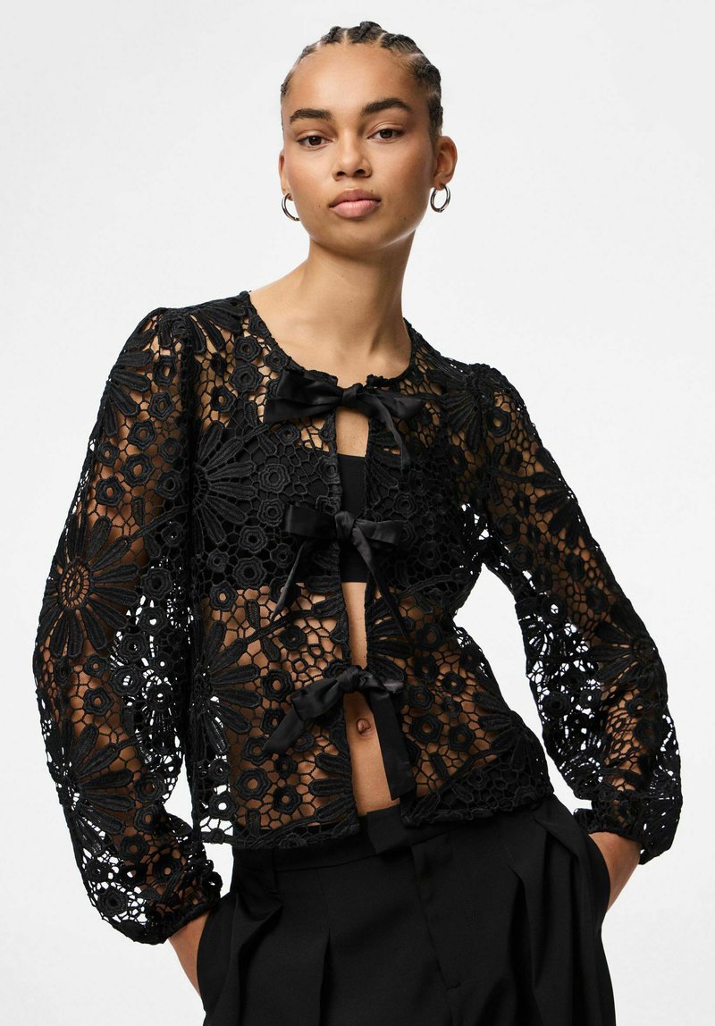 Svart blondercardigan med blomsterpatroner, med lange ermer og knytninger foran. Designet er gjennomsiktig og viser en teksturert overflate.