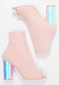 Botines de punto rosas con puntera abierta y tacón cuadrado holográfico. La textura es suave, con un patrón acanalado en la parte superior.