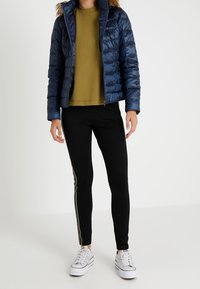 Laivaston sininen toppatakki, jossa on turkiskaistalein somistettu huppu, oliivinvihreä neulepaita, mustat legginsit sivuraidalla ja valkoiset tennarit.