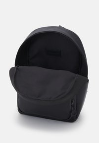 Svart ryggsäck med zippered öppning. Mjuk tygkänsla, rundad form och ett lock. Insidan är enfärgad svart med en märkesetikett.