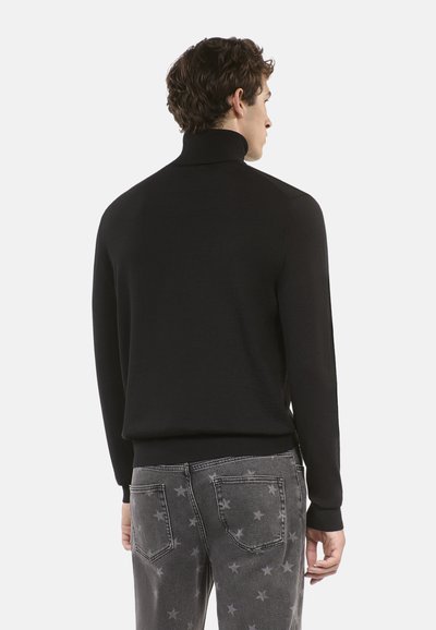 Maglione nero a collo alto con una texture liscia e design aderente, abbinato a jeans grigi con motivi di stelle bianche e taglio slim-fit.