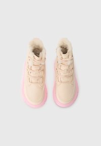 Lys beige ankelstøvler med kunstig pelsfôr, kremfargede snøringer og en rosa gummisåle. Har rund tå og polstret krage for komfort.