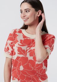 Knit sweater with a floral pattern in coral and cream. Features short sleeves and a ribbed neckline. Soft texture and relaxed fit.