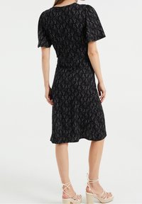 Svart klänning med ett mönstrat mönster, korta puffärmar, figurnära midja och flödande kjol. Matchas med ljusa remsandaler med kilklack.