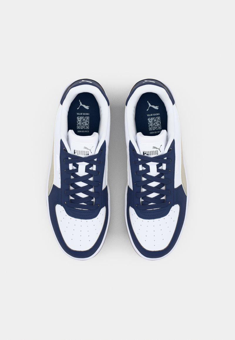 Baskets blanches et navy avec un pare-chocs avant texturé blanc, des lacets navy et une touche dorée. Logo PUMA sur le côté latéral et sur la languette.