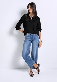 Blusa nera, morbida e con scollo a V, abbinata a jeans chiari a gamba larga. Le calzature presentano una stampa leopardata con un design di cinturini neri.