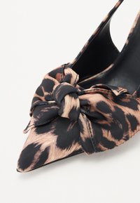Spiss tå høyhelte sko laget av svart stoff med leopardmønster. Har en knyttet sløyfedetalj foran, glatt tekstur og elegant design.