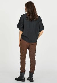 Czarny strukturalny oversize'owy top w połączeniu z brązowymi spodniami cargo z kieszeniami i elastycznymi ściągaczami na kostkach, dopełniony czarnymi sznurowanymi botkami.