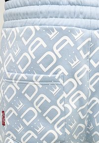 Light blue fabric shorts featuring a repeating white logo pattern and crown motifs, with an elastic waistband and a back pocket.
