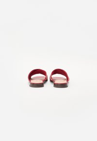 Sandales en toile rouge avec une semelle lisse et plate, présentant un design de lanières entrecroisées. Construction minimaliste et ouverte.