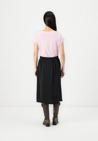 T-shirt rosa chiaro con maniche arrotolate, abbinato a una gonna nera al ginocchio. Stivali marroni al ginocchio con fibbie. Tessuto dalla consistenza liscia.