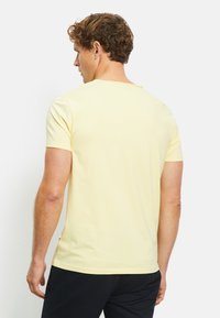 T-shirt giallo a maniche corte in cotone, caratterizzato da una vestibilità comoda, scollo rotondo e spacchi laterali per facilitare il movimento. Accentuato da un'etichetta all'orlo.