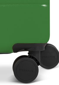 Groene harde koffer met een gladde textuur, voorzien van zwarte wielen en opvallende branding op het wielsoppervlak.