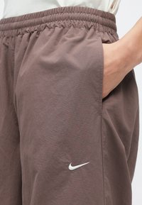Καφέ αθλητικό σορτς από ελαφρύ ύφασμα, με ελαστική μέση και πλαϊνές τσέπες. Λευκό λογότυπο Nike στο κάτω αριστερό μέρος.