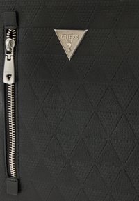 Czarna torebka ze skóry o fakturze, z pikowanym wzorem w kształcie diamentu, srebrnym suwakiem i trójkątnym metalowym logo.