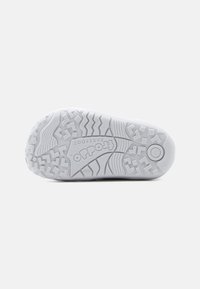 Λευκό καουτσούκ πέλμα παιδικού παπουτσιού που δείχνει υφή πέδης, το εμπορικό όνομα "Froddo" και το μέγεθος "20" χαραγμένα στο κάτω μέρος.