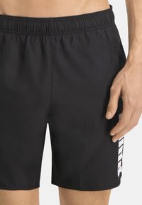 Bañador negro con cintura elástica, con un gráfico lateral en blanco, textura suave y corte hasta la rodilla.