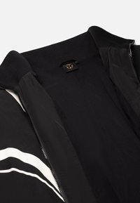 Black bomber jacket with a textured inner lining. Features a high collar, zip closure, and white stripe accents on the front.