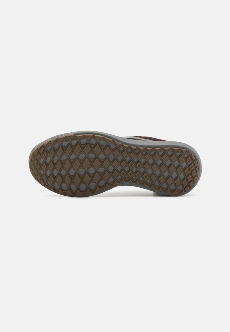 Suela de zapato marrón con un patrón de diamantes para el agarre y un arco ligeramente curvado, sobre un fondo blanco liso.