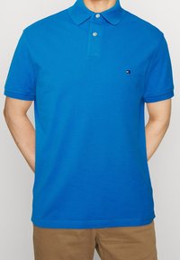 Blå kortärmad polo av bomull, med en treknapplösning, krage och en liten logotyp på bröstet.