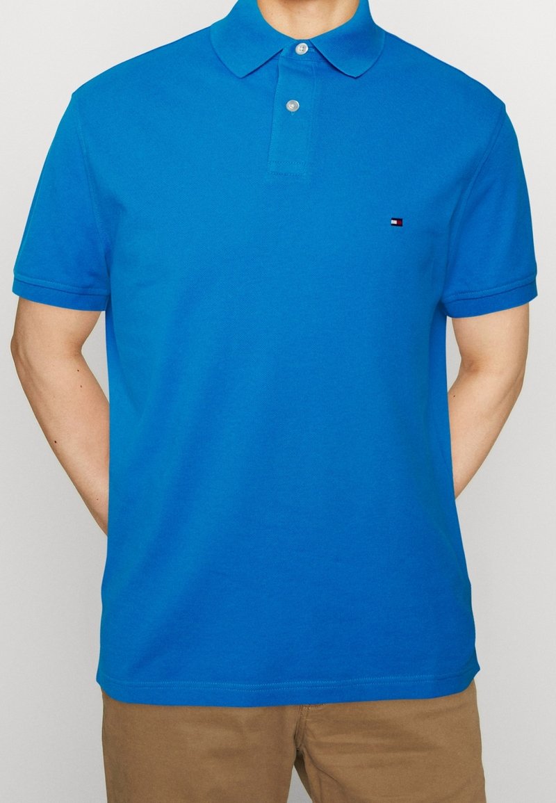 Blå kortärmad polo av bomull, med en treknapplösning, krage och en liten logotyp på bröstet.