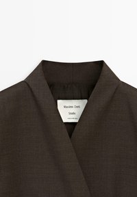 Brauner Stoffkragen mit V-förmigem Design und strukturiertem Finish. Das Etikett trägt die Aufschrift "Massimo Dutti Studio" und weist auf die Herkunft aus Portugal hin.