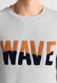 Felpa grigia con collo a giro e lettering oversize testurizzato "WAVE" in arancione e blu navy.