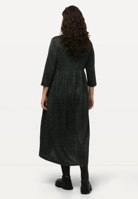 Robe midi noire et scintillante avec une taille froncée, des manches trois-quarts et une jupe fluide. Portée avec des bottes noires chunky.
