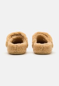 Een paar lichtbruine, donzige instapslippers gezien vanuit de achterkant, met een zachte, wolachtige textuur en gevoerde zolen.