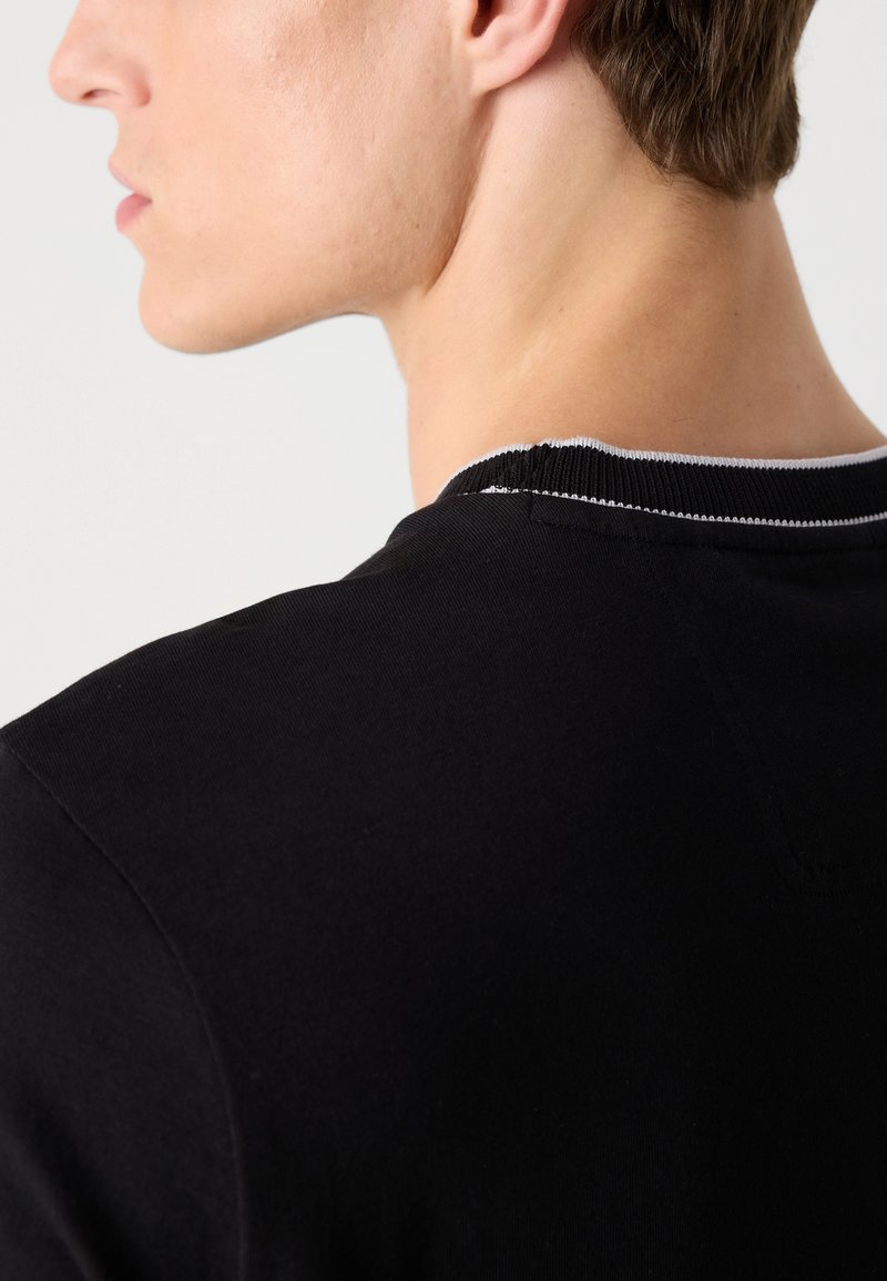 T-shirt noir en coton avec un col rond et des coutures contrastées autour du col. Texture lisse et coupe décontractée.